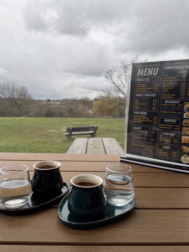 Two coffees on an outdoor table with open parkland behind