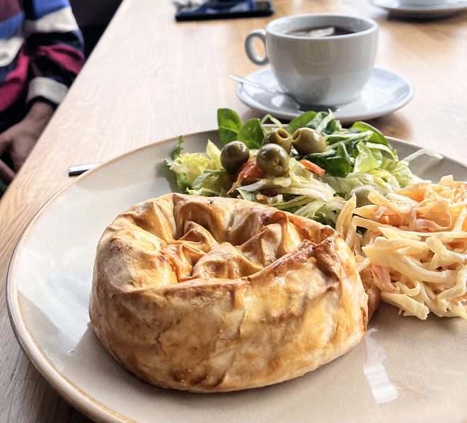 A close-up of a golden pie with salad and chips