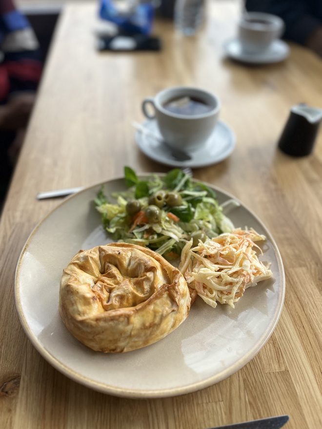 A pie with salad and chips beside a coffee indoors