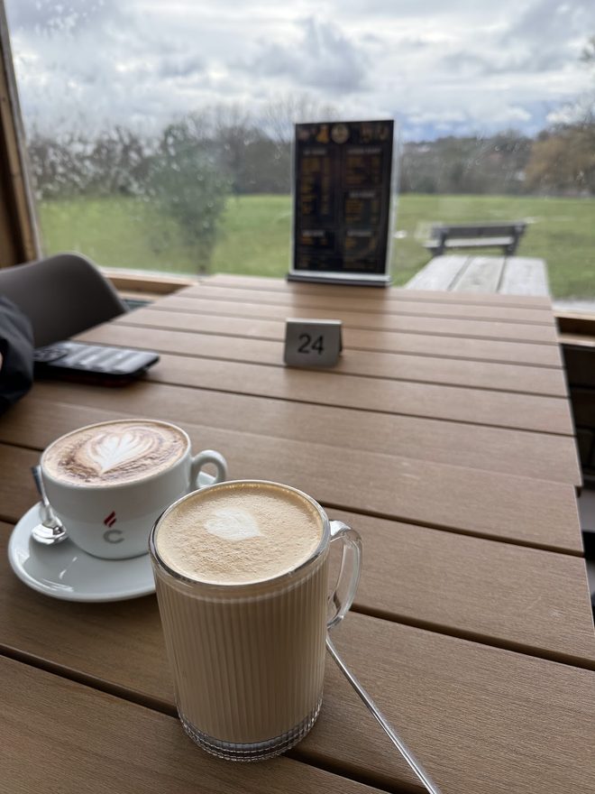 A cappuccino and a latte glass on an outdoor wooden table