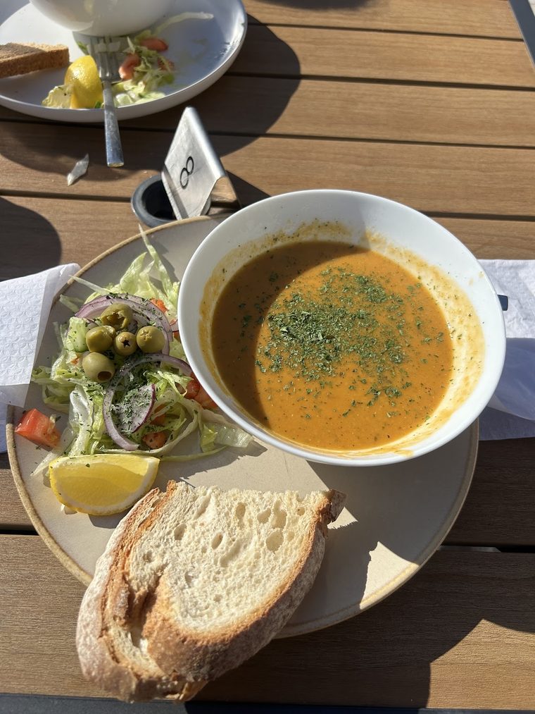A bowl of soup with a side salad and rustic bread