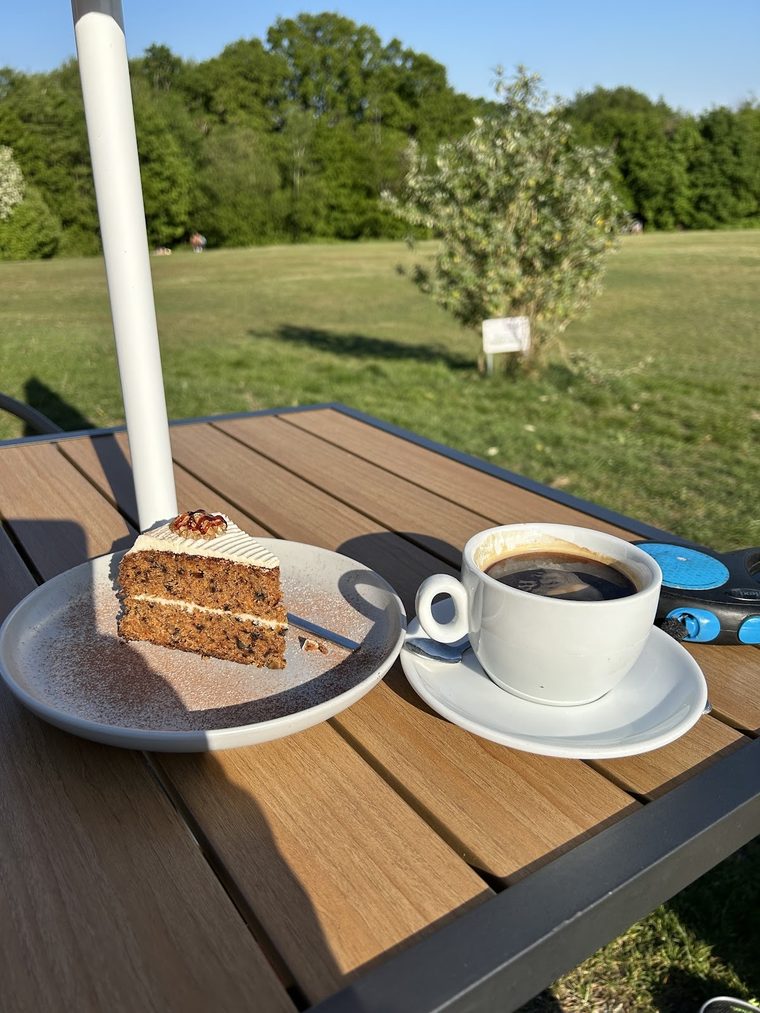 A slice of carrot cake with a black coffee on an outdoor table
